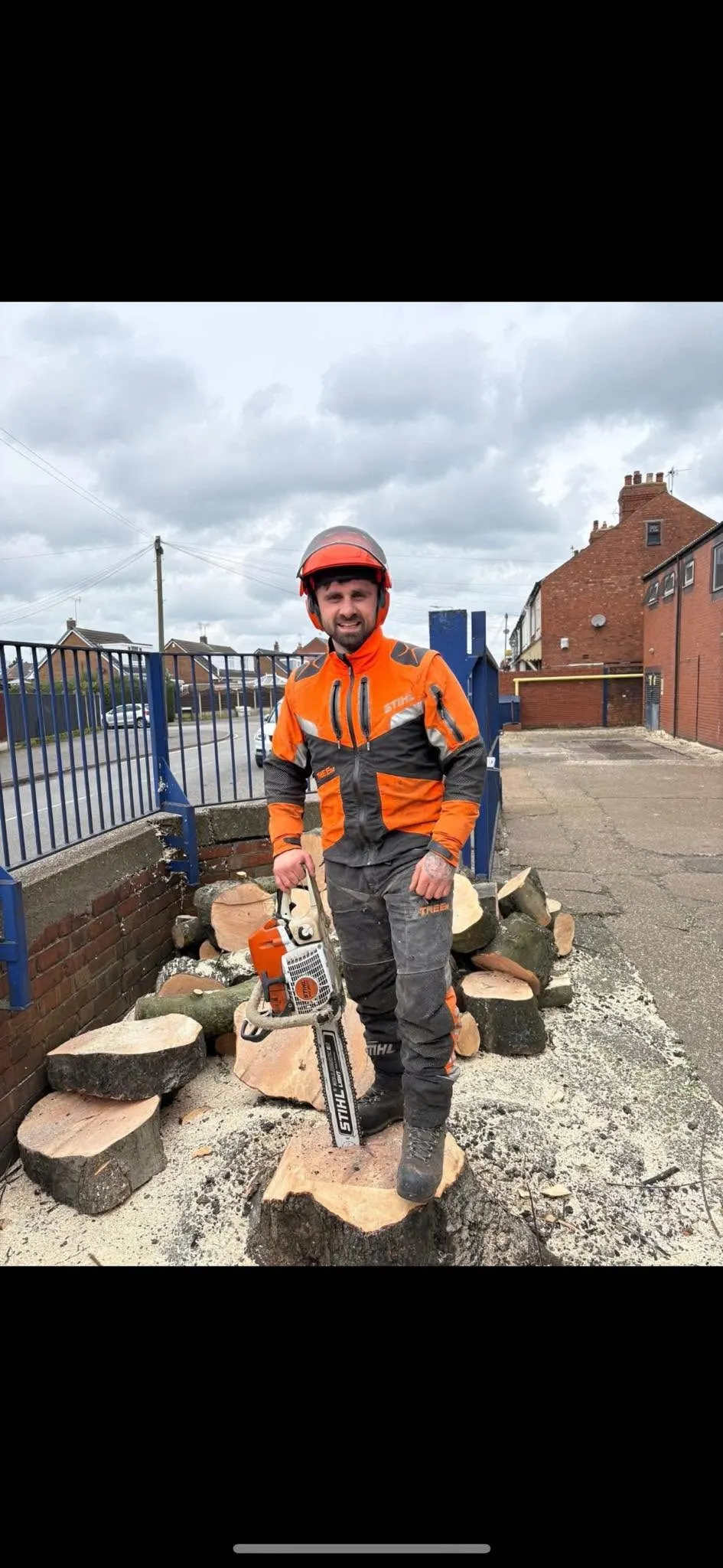 Tom, owner of TB Tree Care, in full PPE with a chainsaw beside a felled tree
